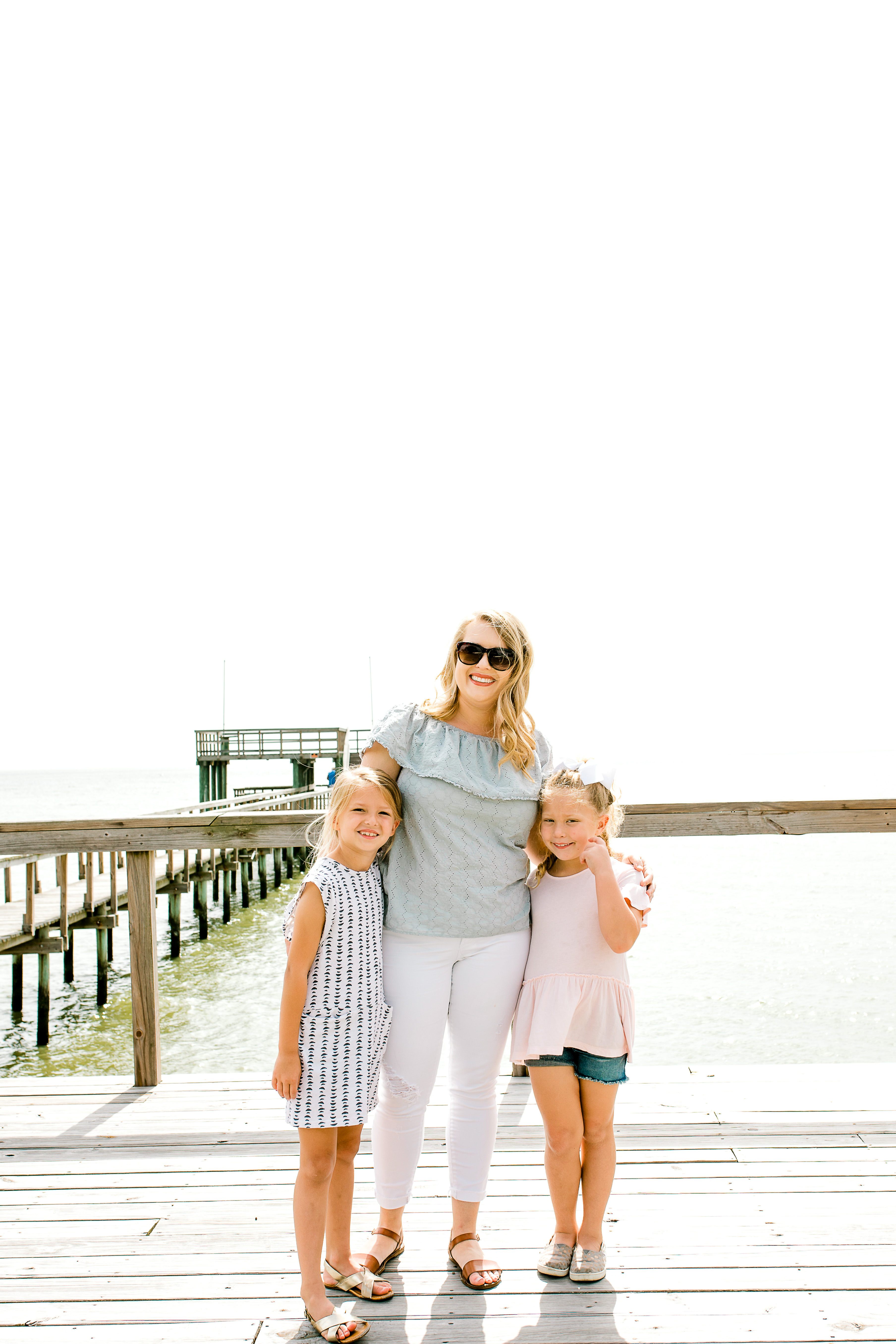 Mom and daughters smiling together on dock near beach. 